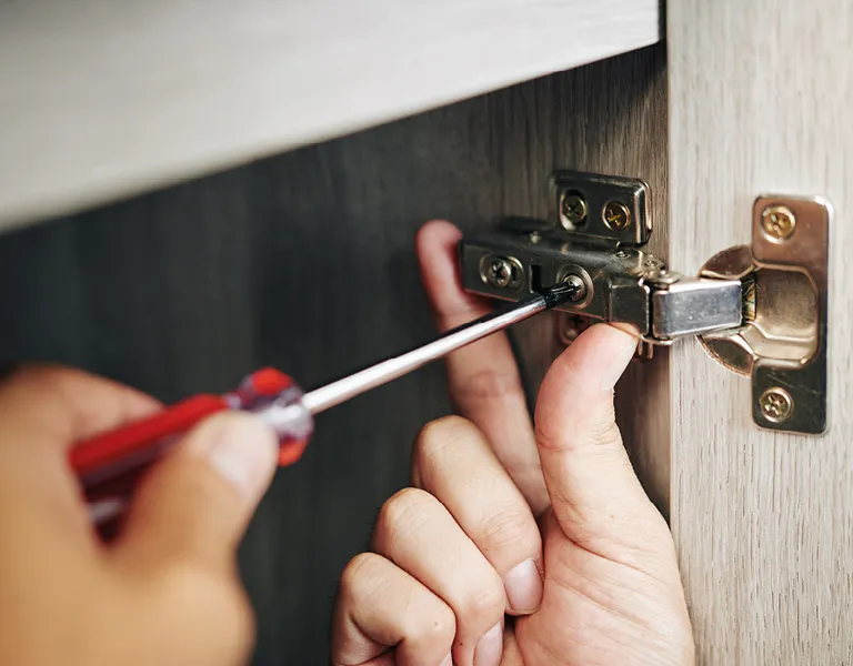 Handwerker montiert präzise ein Scharnier an einem Küchenschrank mit Schraubendreher, zeigt professionelle Küchenmontage und handwerkliche Qualitätsarbeit.